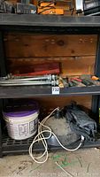 Shelf with large metal farm gate hinges, various hand tools including hammers, pipe wrench, crowbar, mallet, and bolts and nuts.