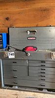 Front view of gray metal Craftsman tool chest on wooden surface, upper lid closed with pliers on top.
