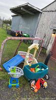 Photo showing hockey net, toddler slide, wagon, shopping cart, and toy trucks on gravel near barn.