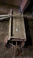 Photo of vintage wooden wagon on dirt floor showing rectangular body and rusted metal wheels.