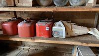 Three red portable fuel tanks and left portion of white outboard motor on wooden shelf