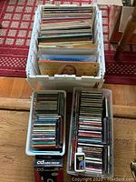 Box filled with approximately 75 vinyl records with visibly colorful and vintage album covers, two bins holding around 100 CDs each, and CD cleaning accessories visible.