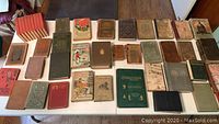 Wide overview of 34 antique books laid flat on a table, showing various sizes, covers, and wear conditions.