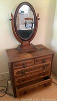 Full front view of walnut chest of drawers with attached oval mirror.