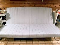 White futon sofa bed in upright sofa position on tiled floor with wooden wall background.