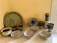 Full set of pottery items arranged: large platter at back, wine carafe with cork, four cups, serving bowl, four smaller bowls and small planter.