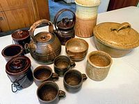Overview of most pottery pieces on white surface, including teapots, four matching cups, smaller jars, and cups.