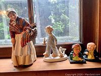 Photo showing all four figurines including Grandma, child with dog, Mr. Pickwick bust, and female bust together on a window sill.