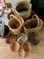 Twelve baskets of various shapes and sizes displayed on floor and table, showing antique basket with lid, bread baskets, and small baskets.