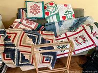 Five quilts visible along with two pillows and a wooden quilt rack. The antique green and red tulip quilt is identifiable by its tulip pattern and color.