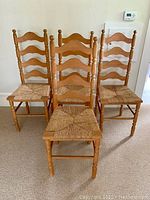 Front view showing all four wooden ladder back chairs with woven seats arranged in a group on carpeted floor.