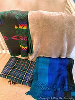Four blankets displayed: Pendleton wool blanket with bright geometric design, light brown fleece blanket, Scottish plaid wool blanket, and blue-green striped wool throw.