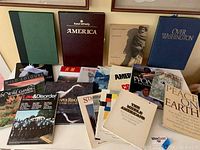 17 coffee table books arranged on floor and a low table, titles visible include America by Rand McNally, Over Washington, Peace on Earth, Law & Disorder magazine, The Wild Garden by Violet Stevenson among others.