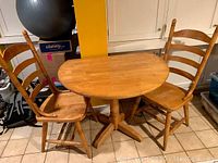 Two wood chairs positioned on either side of a round wood table with folding leaves. Shows overall set appearance.