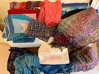 13 scarves and pashminas laid out showing variety of colors and textures including red, blue, pink, and multi-color designs.