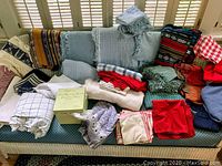 Full assortment of tablecloths, napkins, and runners shown on couch, various textures and colors visible