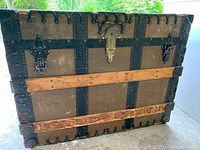 Front view of the antique steamer trunk showing wood slats, metal reinforcements, metal lock and clasps, and scalloped metal trim.