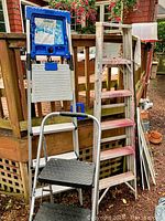 Three ladders stacked/placed together: blue and silver Cosco 10 ft ladder folded, older wooden Safety Master 8 ft ladder with paint spots, and Cosco 3-step step ladder with black steps in front.