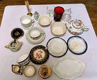 Overall view of the various antique dishes, cups, plates, glassware including Lenox cup, Paragon cup and saucer, dishes and glass items displayed on a white surface.