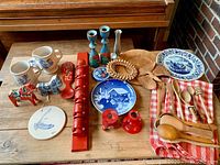 Full overview of assorted items on wood table showing plates, spoons, decorative candle holders, and carved wooden pieces.