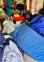Green rolled tent with orange interior, sleeping bags, blue air mattresses, and assorted gear displayed on floor and couch.
