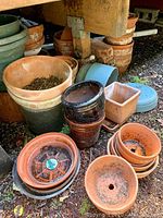 Multiple garden pots stacked including terracotta, plastic, and ceramic with some containing soil and some stacked inside each other