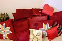 Multiple red and one yellow pillow with ethnic patterns and solid colors piled together, showing variety in size and design.