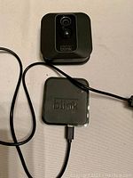 Blink camera and sync module connected by power cables on white surface