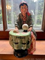 Front view of the Royal Doulton fortune teller figurine showing the woman with a red headscarf, crystal ball, and detailed tablecloth.