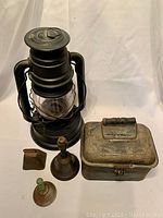 Overview photo of all five items: lantern, lunch box, two larger bells, and a smaller bell, placed on white backdrop.