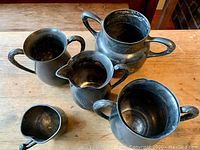Overall set of five antique pewter pieces arranged on wooden table, showing shapes and handles.