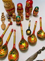 Photo of Russian nesting dolls arranged upright alongside 8 painted wooden spoons and 1 carved wooden utensil.