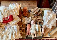Full overview of trunk, dolls, garments, lace and accessories arranged on wooden surface