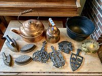 Full view of all items including brass kettles, cast iron door stops, trivets, irons, and cast iron kettle