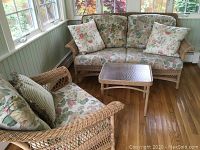 Full view of loveseat, armchair, small table and coffee table arranged in sunroom.
