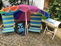 Wide shot showing two striped beach chairs, colorful beach umbrella, blue LLBean soft cooler, and small folding side patio table.