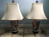 Two matched Asian porcelain ginger jar table lamps with floral pattern, cream silk shades, brass finials on wood bases, placed side by side
