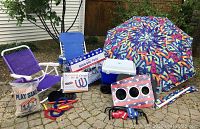 Two purple folding beach chairs with white frames, full horseshoe set with red and blue horseshoes, bag of Robel play sand, cornhole bean bag toss box, white and blue rolling cooler, and colorful patterned beach umbrella.