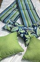 Photo showing two large striped chair cushions and four accent pillows in green and leaf pattern on white background.