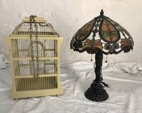 Image showing vintage cream birdcage and Tiffany-style lamp side by side on white surface