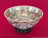 Large hand-painted Chinese porcelain bowl angled to show exterior and depth on wood stand against red cloth background.