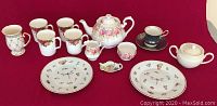 Full view of all items arranged on red cloth background including plates, cups, teapot, sugar bowl, creamer, and teapot-shaped dish.