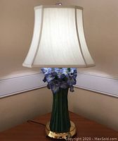 Full view of the lamp showing the tapered white silk lampshade, green resin iris stem base, and polished brass base.