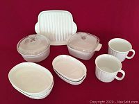 Full set of Corningware oven-to-table cookware displayed on red background including casseroles, baking dishes, platter and cups.