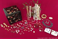 Wide assortment of costume jewelry laid out on red fabric including earrings, rings, brooches, three watches, and the lacquered jewelry box