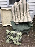 Green vinyl wicker side table with cushions arranged on and around it, including floral and striped seat cushions and a tufted pillow.