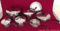 Full set of stainless steel Farberware pots and pans shown with lids and handles on a red background, showcasing different sizes and shapes