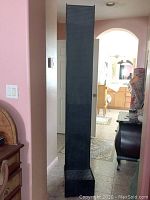 Photo showing front view of tall black glossy resin water fountain placed indoors in a hallway.