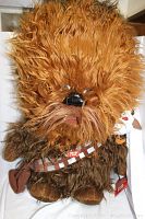 Front and partial side view photo of the Chewbacca talking plush, showing its detailed, long brown fur, facial features, and brown bandolier.