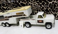 Full side view of white Tonka truck attached to the 5th wheel camper showing the camper door open and articulation point